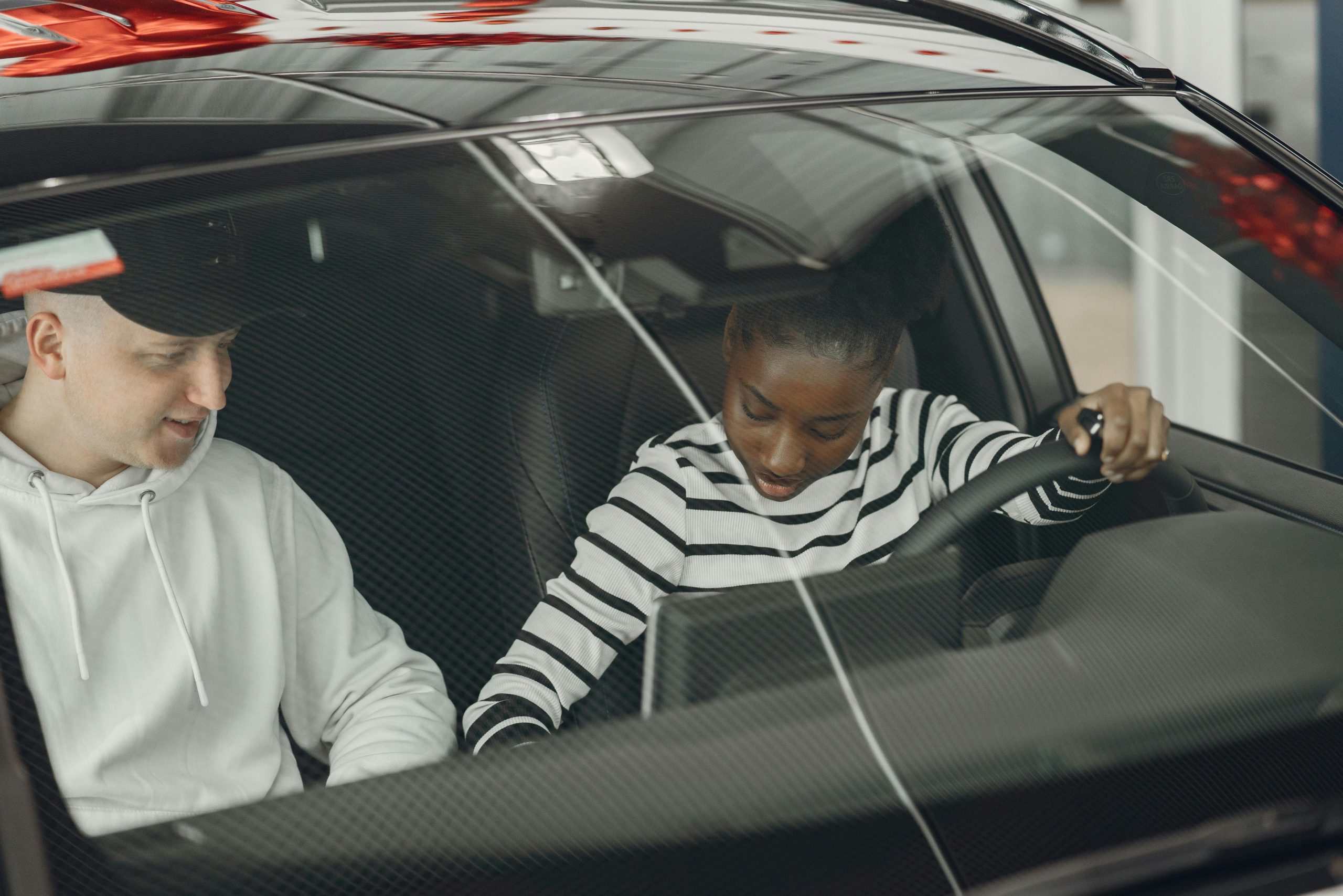 Black woman and caucasian man sitting inside a vehicle, discussing driving.
