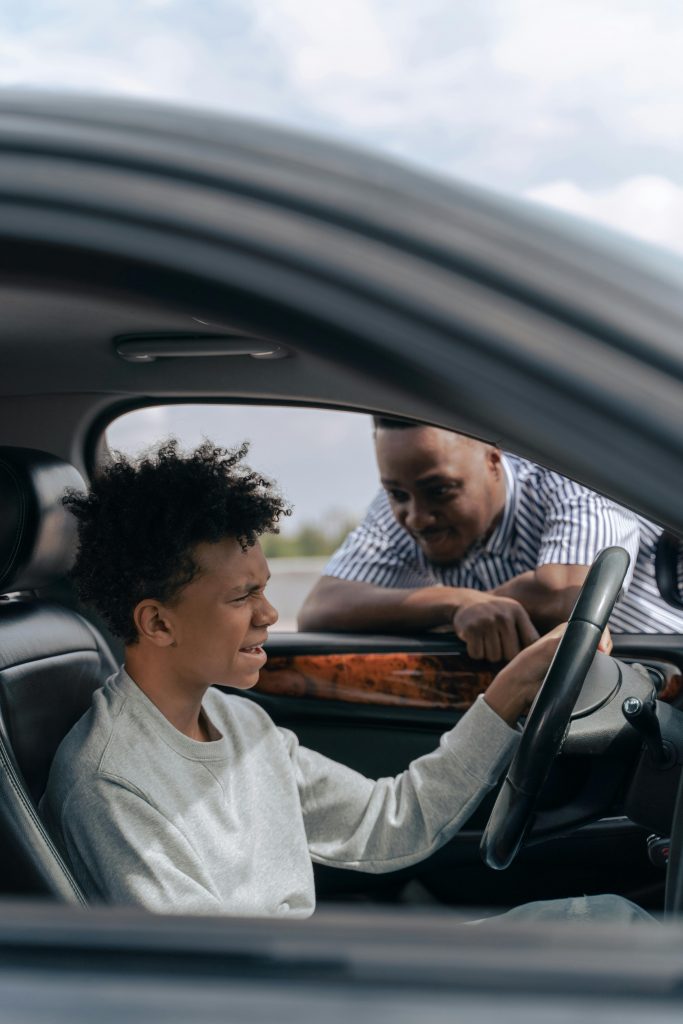 Father instructs son in car driving lesson inside a vehicle on a sunny day.